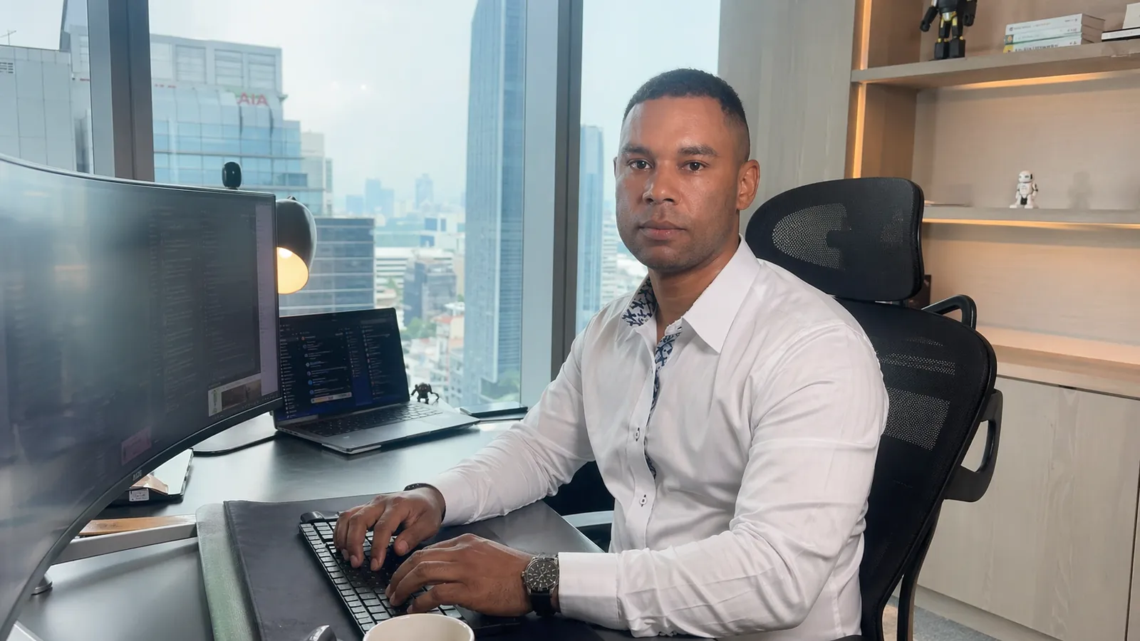 Billy Reiner at his desk — multi-monitor workstation, city skyline behind him.